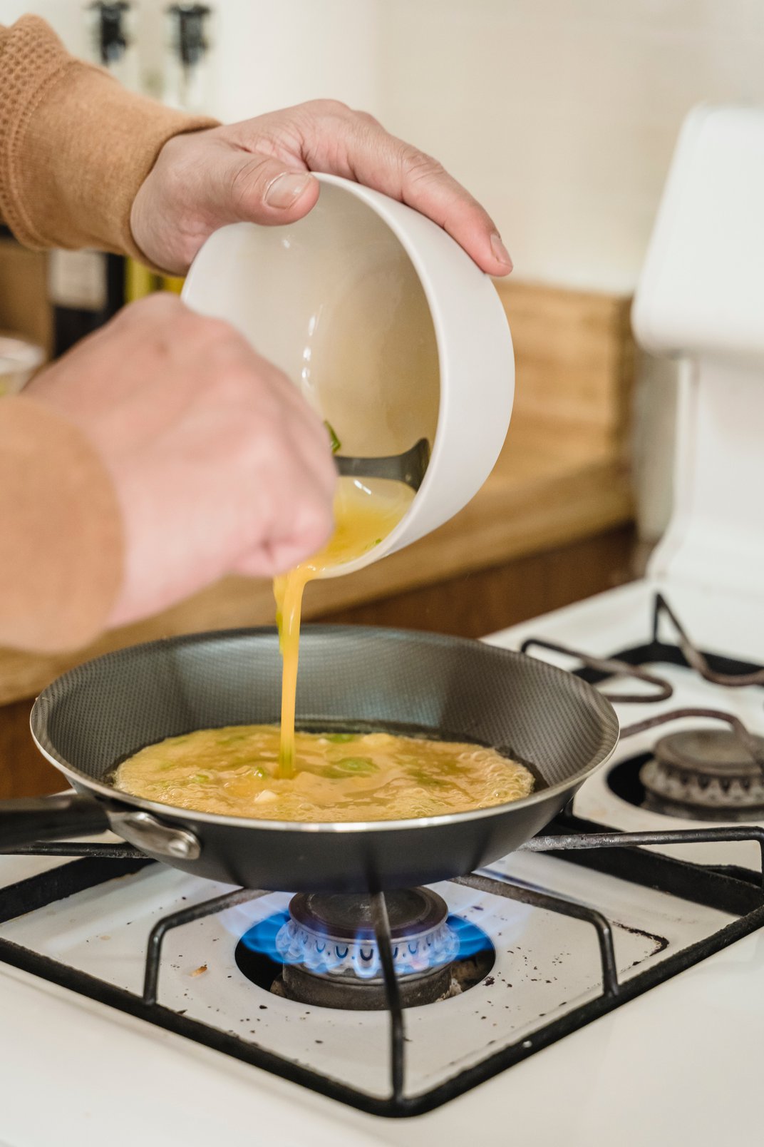 Person cooking scrambled eggs on white gas stove